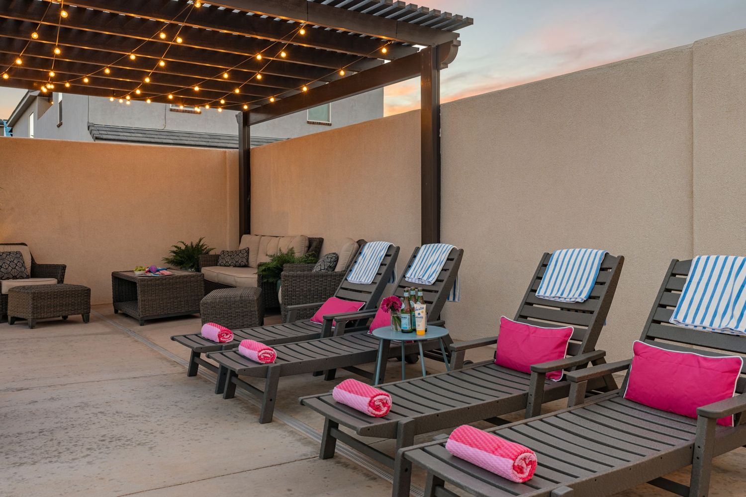 Loungers with pink pillows under a string-lit pergola